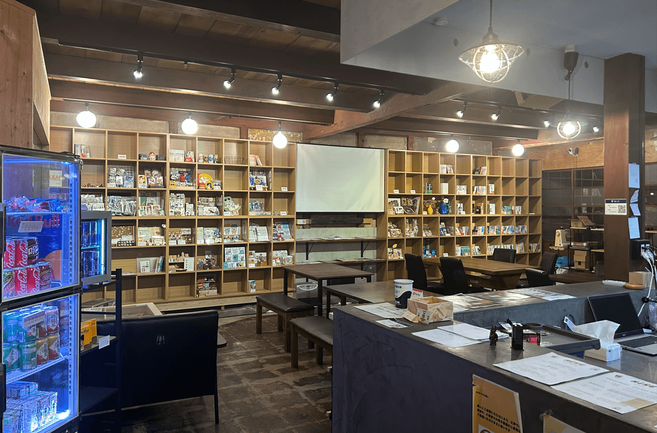 棚とテーブル、スクリーンが見えるTsunagaRoomの店内
